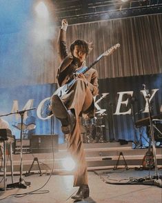 a man is jumping in the air on stage with his guitar and other musical instruments