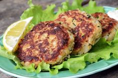 three crab cakes with lettuce and lemon wedges on a green plate, ready to be eaten