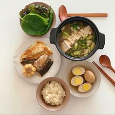 an assortment of food is displayed on a white table with chopsticks and bowls