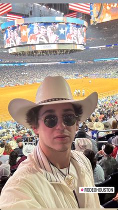 a man wearing a cowboy hat and sunglasses in front of an arena at a baseball game