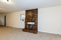 an empty living room with a brick fireplace in the center and door to another room