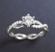 a white gold engagement ring with a twisted band and a round diamond center, on a dark background