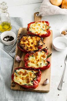 four stuffed bell peppers on a cutting board with garlic and seasoning in the background