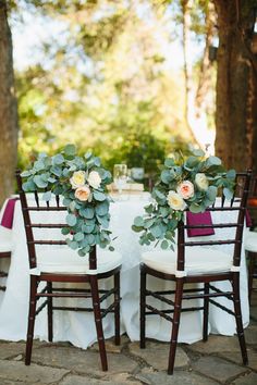 two chairs with flowers and greenery on them are set up for an outdoor wedding