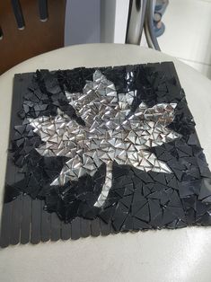 a black and silver mosaic tile with a leaf on the top, sitting on a chair