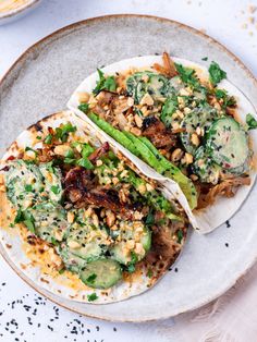 two tacos on a plate topped with meat and veggies, garnished with seasoning