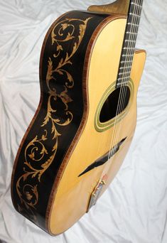 an old acoustic guitar is sitting on a white cloth covered sheeted surface with a black and gold design