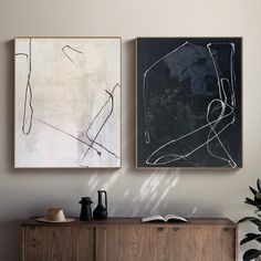 two paintings hang on the wall next to a sideboard with books and vases