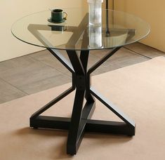 a glass table with metal legs and a vase on the top, in front of a beige wall