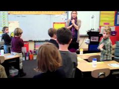 a group of children standing in front of a whiteboard with an adult talking to them