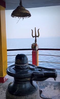 a large metal object sitting on top of a boat near the ocean with a bell hanging from it's side