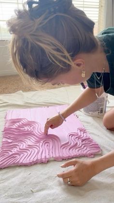 a woman is painting a piece of art with pink paint on the floor in front of a window