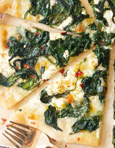 several slices of pizza with spinach and cheese on top, next to a fork