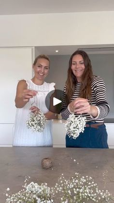 two women standing next to each other in front of a table with flowers on it