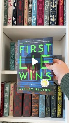 a person holding up a book in front of a bookshelf