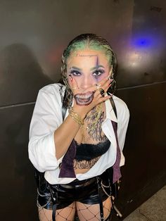 a woman with makeup and piercings on her face posing for the camera in front of a wall