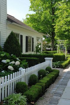 a white picket fence in front of a house with trees and bushes on the side