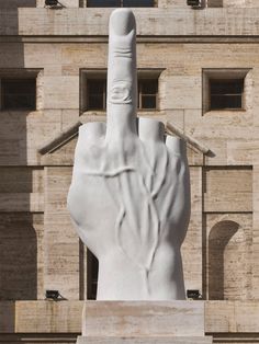 a large white statue with a hand pointing towards the sky in front of a building