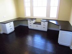 an empty room with white cabinets and black counter tops on the floor, in front of a window