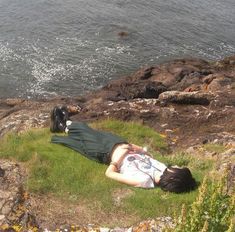 a man laying on top of a lush green field next to the ocean