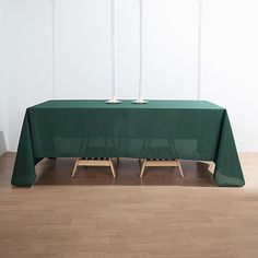 a table with two candles on it in front of a white wall and wooden floor