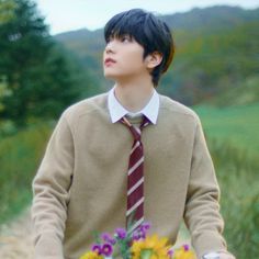 a young man wearing a sweater and tie holding a bouquet of flowers in his hands