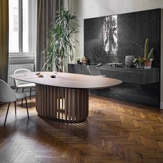 a dining room table with chairs and a plant in the corner next to it on top of a hard wood floor