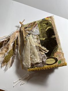 an altered book is sitting on a table with fabric and laces around the edges