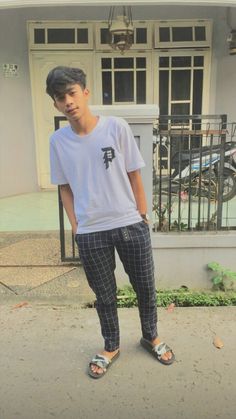 a young man standing on the sidewalk in front of a building with his feet up