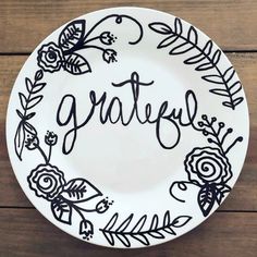 a white plate with black lettering that says grateful on it, surrounded by flowers and leaves