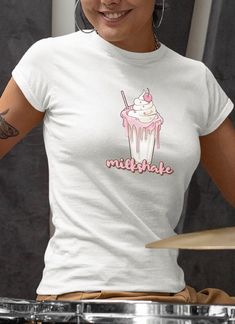 "Introducing our Women's Milkshake T-Shirt, a deliciously delightful ode to the timeless joy of milkshakes! This t-shirt is designed to celebrate the sweetness and nostalgia that comes with sipping on a classic milkshake. Featuring a charming and whimsical design, this t-shirt showcases a vibrant illustration of a tall, frosty milkshake glass and a perfectly placed cherry on top. The playful typography completes the design, spelling out \"Milkshake\" in a fun and eye-catching way. .: 100% ringspun cotton (fiber content may vary for different colors) .: Light fabric (4.5 oz/yd² (153 g/m .: Semi-fitted .: Tear-away label .: Runs true to size For more designs please visit our shop, thank you. https://www.etsy.com/shop/GoodsbyGladney" Sweet White Short Sleeve T-shirt, Sweet White T-shirt With Funny Print, White Sweet T-shirt With Funny Print, Sweet White T-shirt With Graphic Print, Sweet T-shirt For Summer Gift, Sweet Summer T-shirt As Gift, Sweet Crew Neck T-shirt For Gift, Cream Tshirt, Playful Typography