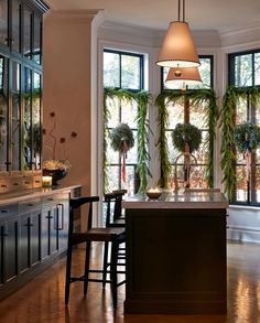 a large kitchen with an island in the middle and lots of plants on the windows