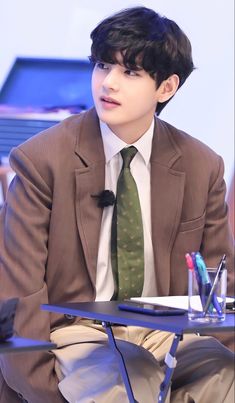 a man in a suit and tie sitting at a table with pens and pencils