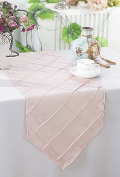 a pink table runner on top of a white table with vases and flowers in the background