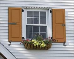 an open window with yellow shutters and potted plants on the ledge below it