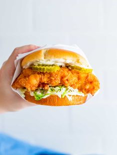 a hand holding a sandwich with chicken and lettuce on it, in front of a white background