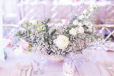 a vase filled with white flowers sitting on top of a table next to silverware