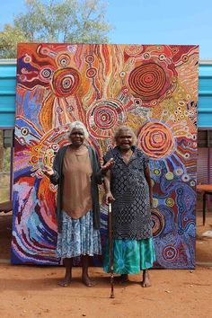 two women standing in front of a colorful painting