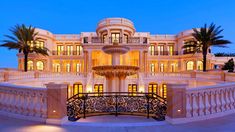 a large mansion with a fountain in front of it at night time and palm trees around the entrance