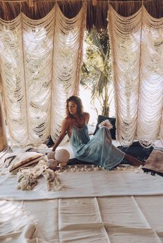 a woman sitting on top of a bed in a room with sheer curtains and pillows