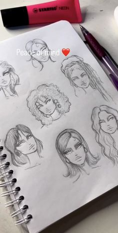 an open notebook with drawings of women's heads on it and a marker next to it