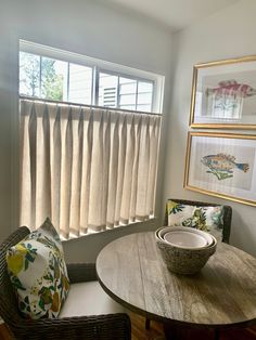 a table with two chairs and a bowl on it in front of a window filled with curtains