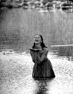 a woman standing in the rain with her hands on her chest and an umbrella over her head