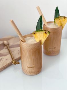 two glasses filled with pineapple drink on top of a wooden tray next to a cutting board