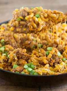 a skillet full of macaroni and cheese being lifted with a wooden spoon