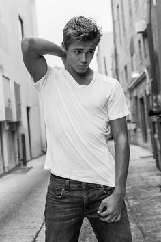 black and white photograph of a young man leaning against a wall with his hand on his head