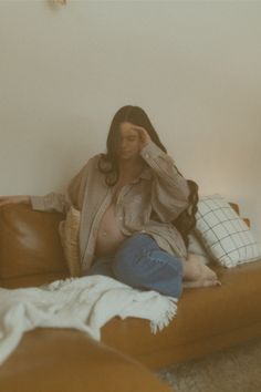 a woman sitting on top of a brown couch next to a white wall and pillows