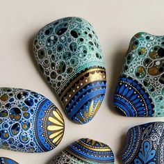 four painted rocks sitting next to each other on a white surface with gold and blue designs