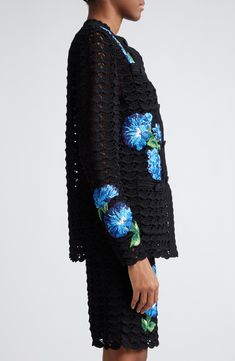 a woman is wearing a black dress with blue flowers on the sleeves and back,