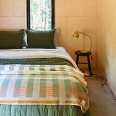 a bed sitting under a window next to a nightstand with a lamp on top of it